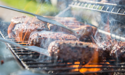 A close-up of hamburgers getting moved with tongs on a grill.